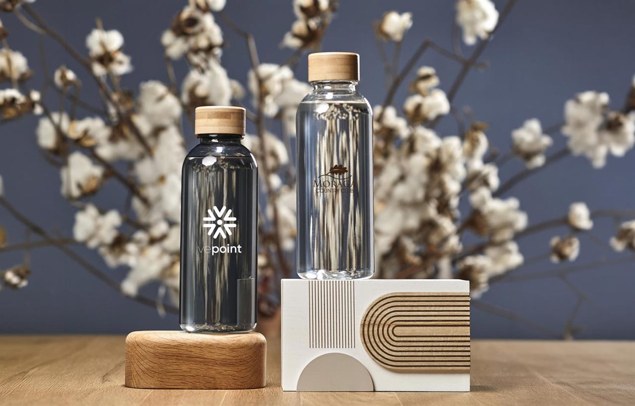 Two branded water bottles with bamboo lids, styled with cotton branches on a wooden surface
